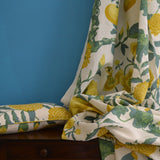 Floral and lemon patterned pillow and fabric draped over a wooden dresser with a blue background.