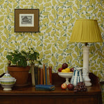Room interior with a wooden sideboard against a patterned wall, featuring a lamp, books, fruit, and a plant.
