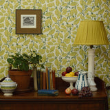 Room interior with a wooden sideboard against a patterned wall, featuring a lamp, books, fruit, and a plant.