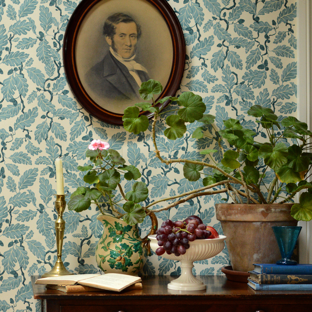 Decorative room interior with floral wallpaper, a portrait, and plants on a wooden table.
