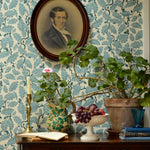 Decorative room interior with floral wallpaper, a portrait, and plants on a wooden table.