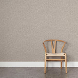 A wooden chair stands in front of a wall papered in a painterly checked pattern in shades of greige.