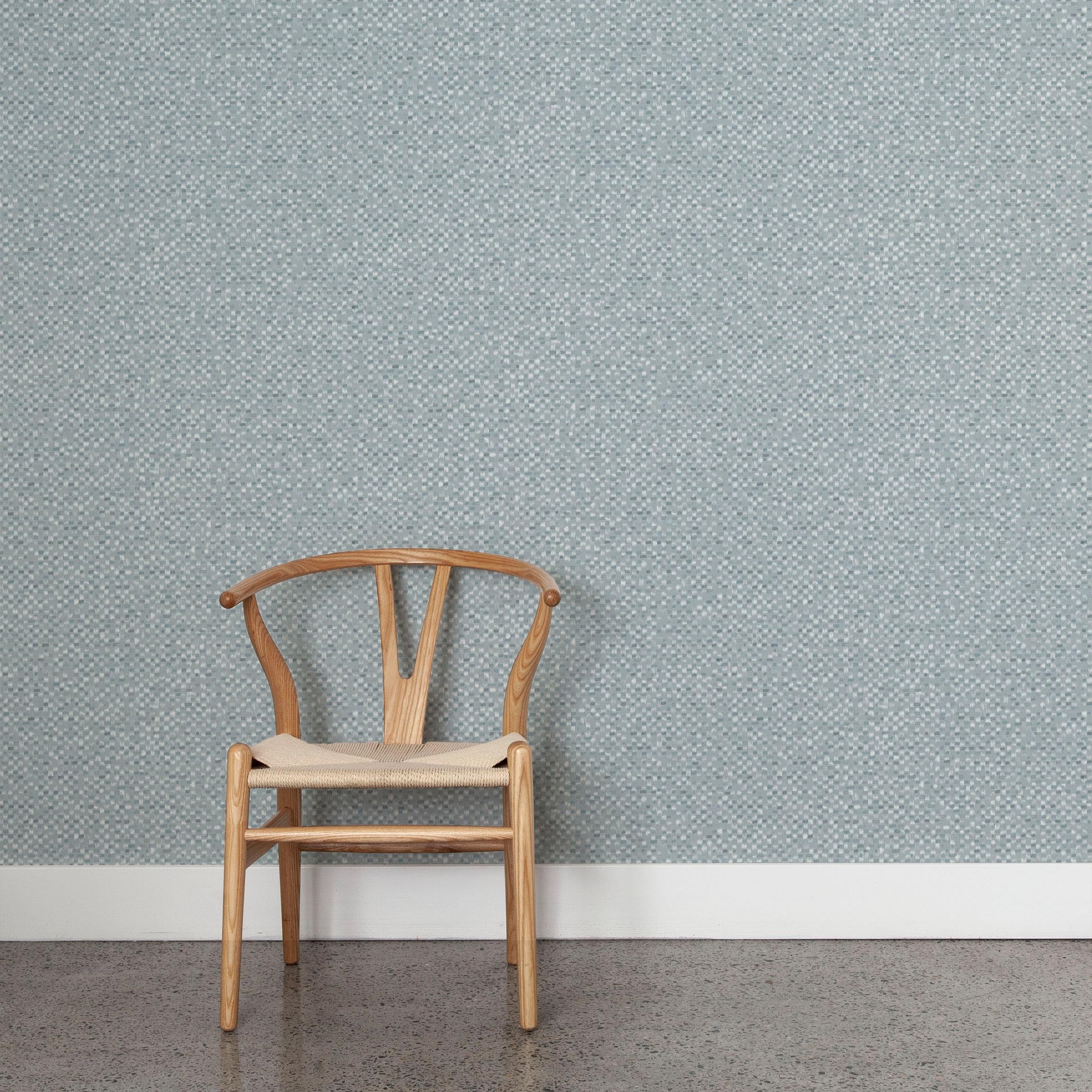 A wooden chair stands in front of a wall papered in a painterly checked pattern in shades of blue and white.