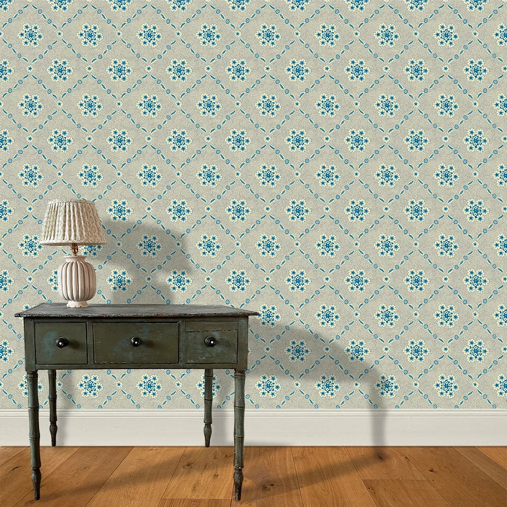 A wooden end table and lamp stand in front of a wall papered in an intricate floral lattice print in blue and tan.