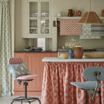 A cozy kitchen space with an island finished with a fabric skirt in a flower and leaf lattice print in red.