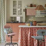 A cozy kitchen space with an island finished with a fabric skirt in a flower and leaf lattice print in red.