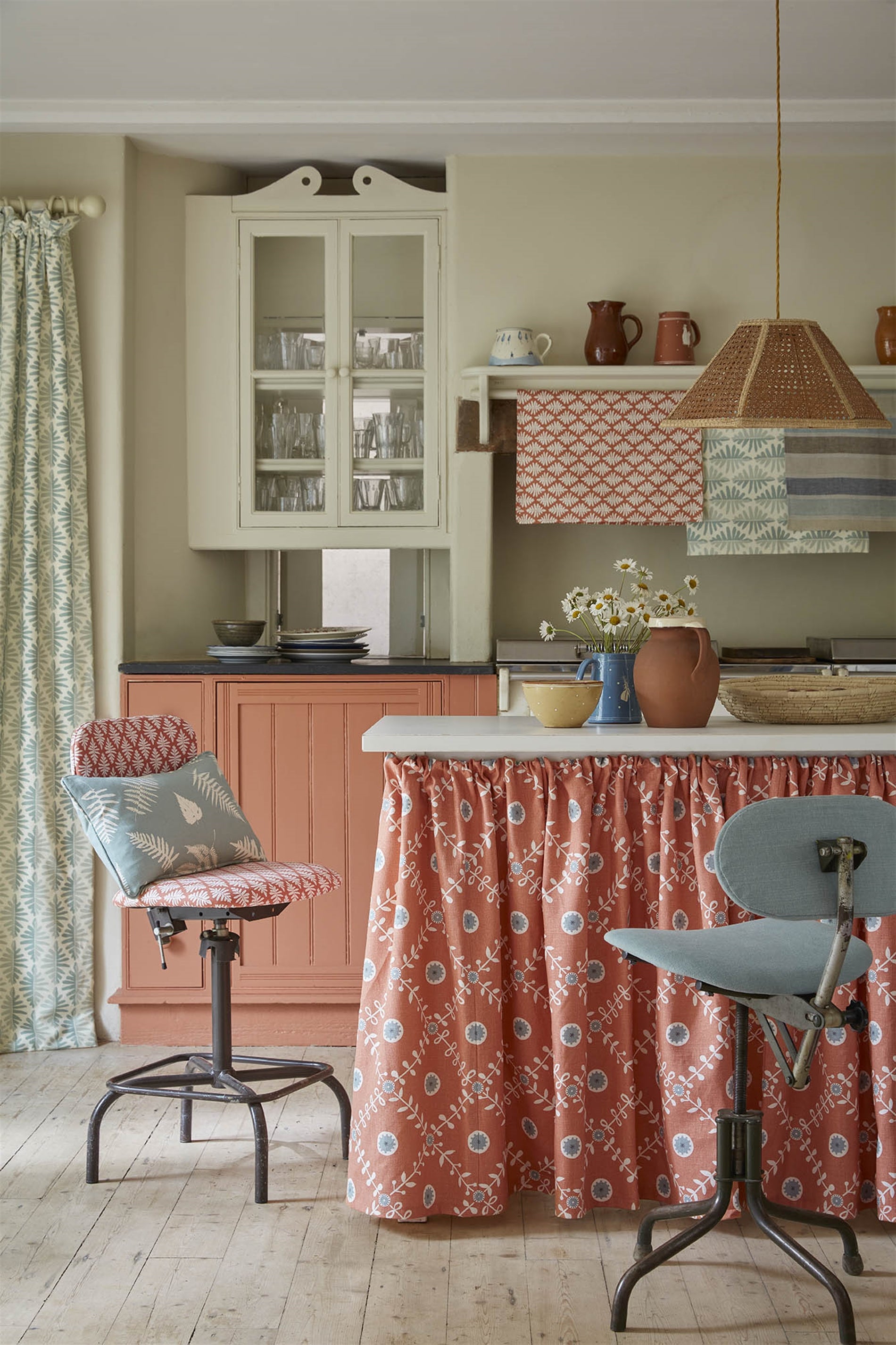 A cozy kitchen space with an island finished with a fabric skirt in a flower and leaf lattice print in red.