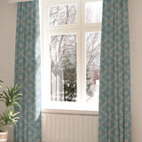 A large, sunny window with long curtains in a flower and leaf lattice print on a blue field.