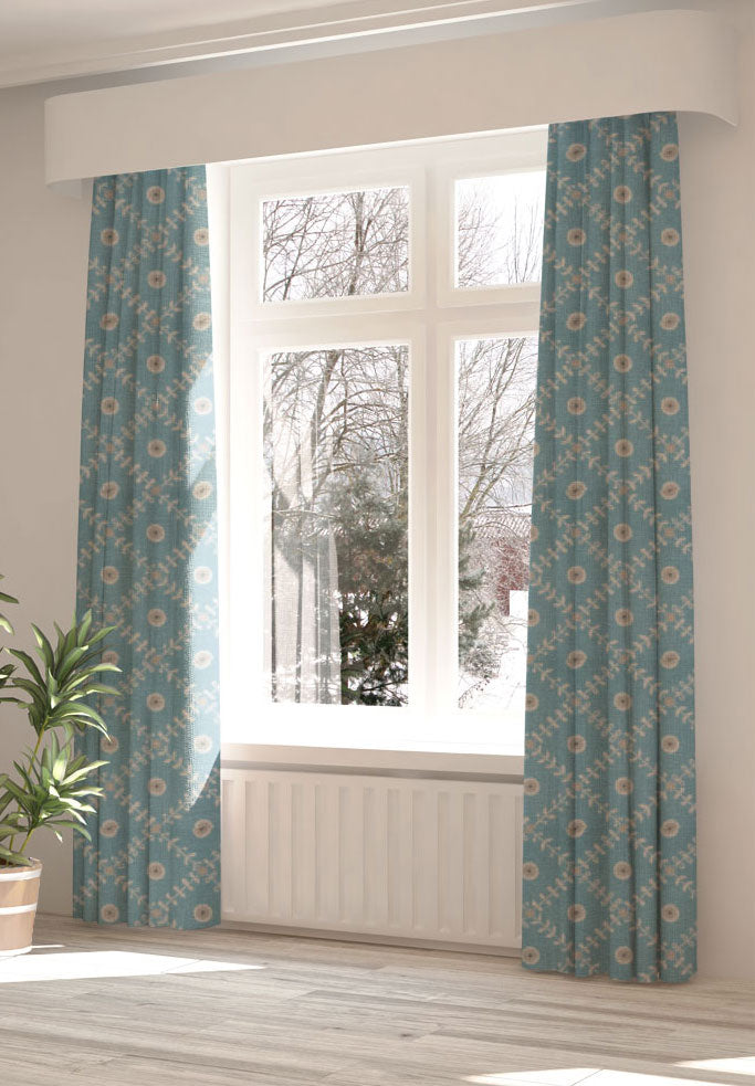 A large, sunny window with long curtains in a flower and leaf lattice print on a blue field.