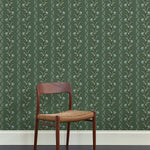 A wooden dining chair against a wallpaper in a painterly botanical stripe pattern in shades of green with blue accents.