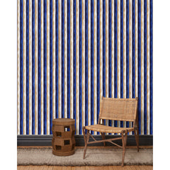 A wooden chair and end table in front of a wall papered in a curvy hand-painted stripe pattern in blue, gold, white and navy.