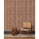 A wooden chair and end table in front of a wall papered in a curvy hand-painted stripe pattern in shades of brown, gold, rust and white.