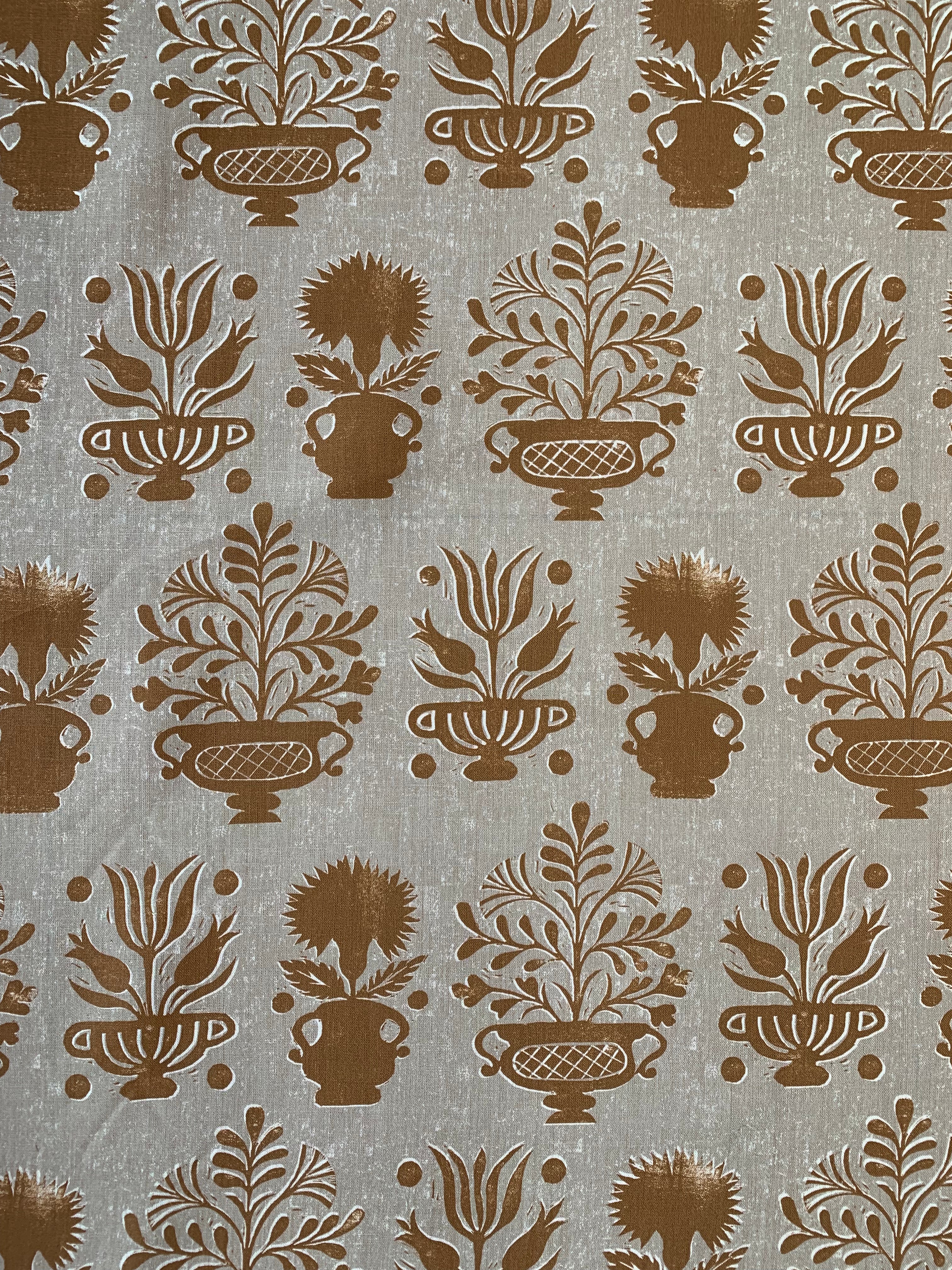 Detail of fabric in a repeating vase and plant print in rust on a mottled cream field.