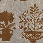 Close-up of fabric in a repeating vase and plant print in rust on a mottled cream field.