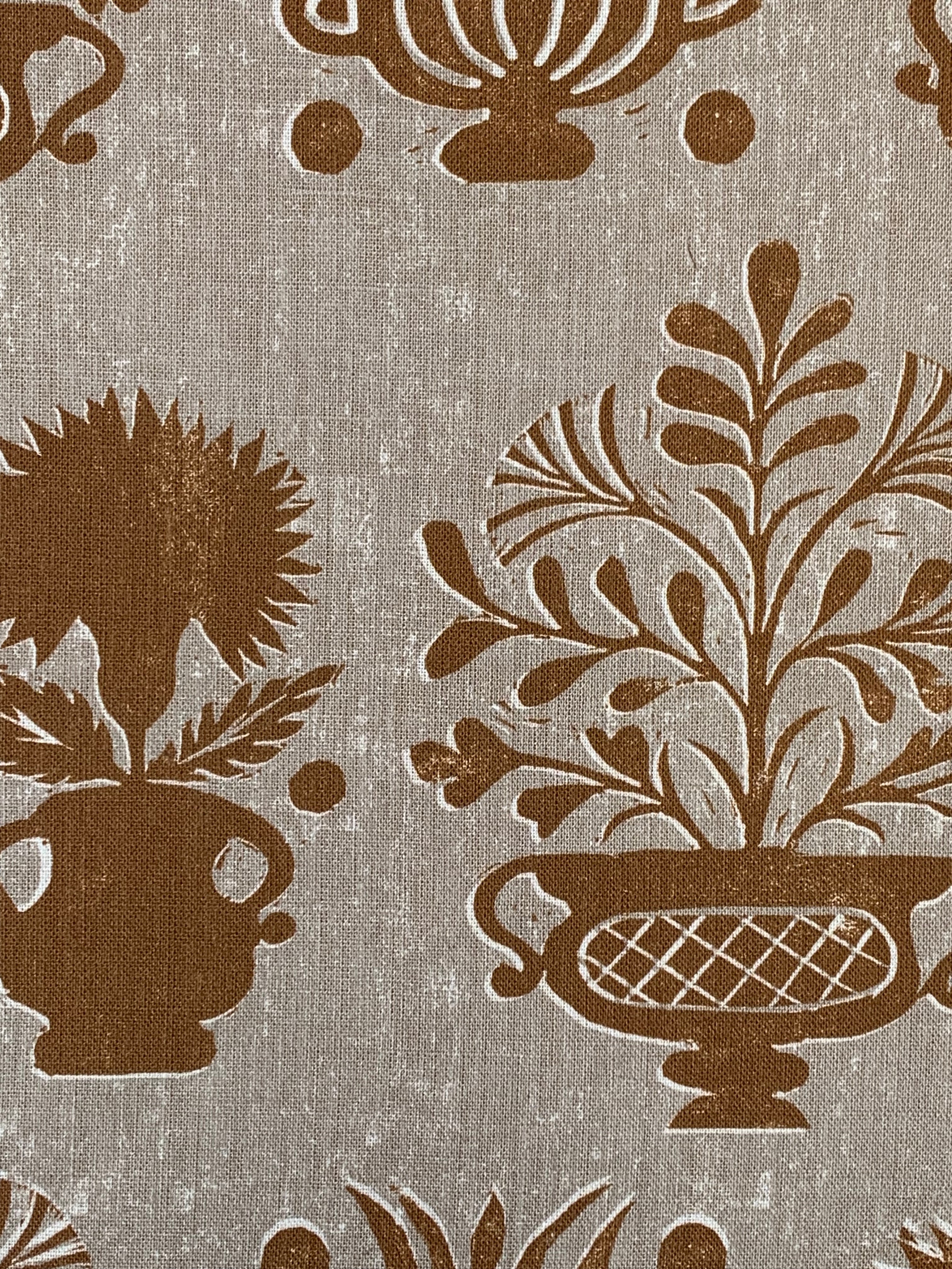 Close-up of fabric in a repeating vase and plant print in rust on a mottled cream field.