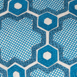 Detail of fabric with a geometric prism pattern embroidered in shades of blue on a white field.