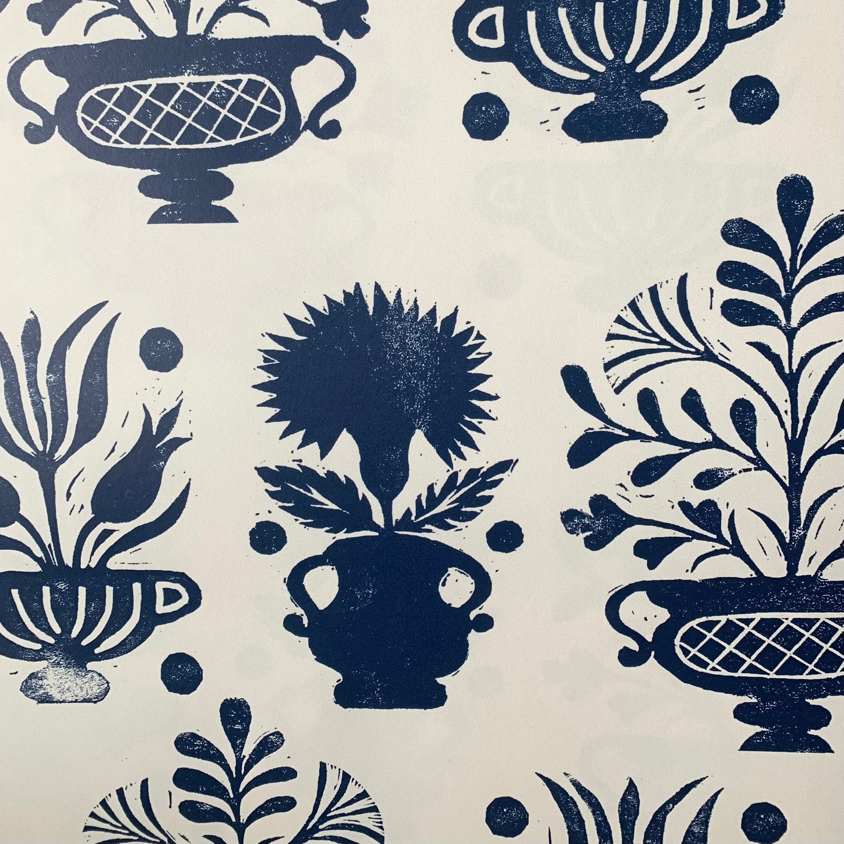 Close-up of wallpaper in a repeating vase and plant print in navy on a cream field.