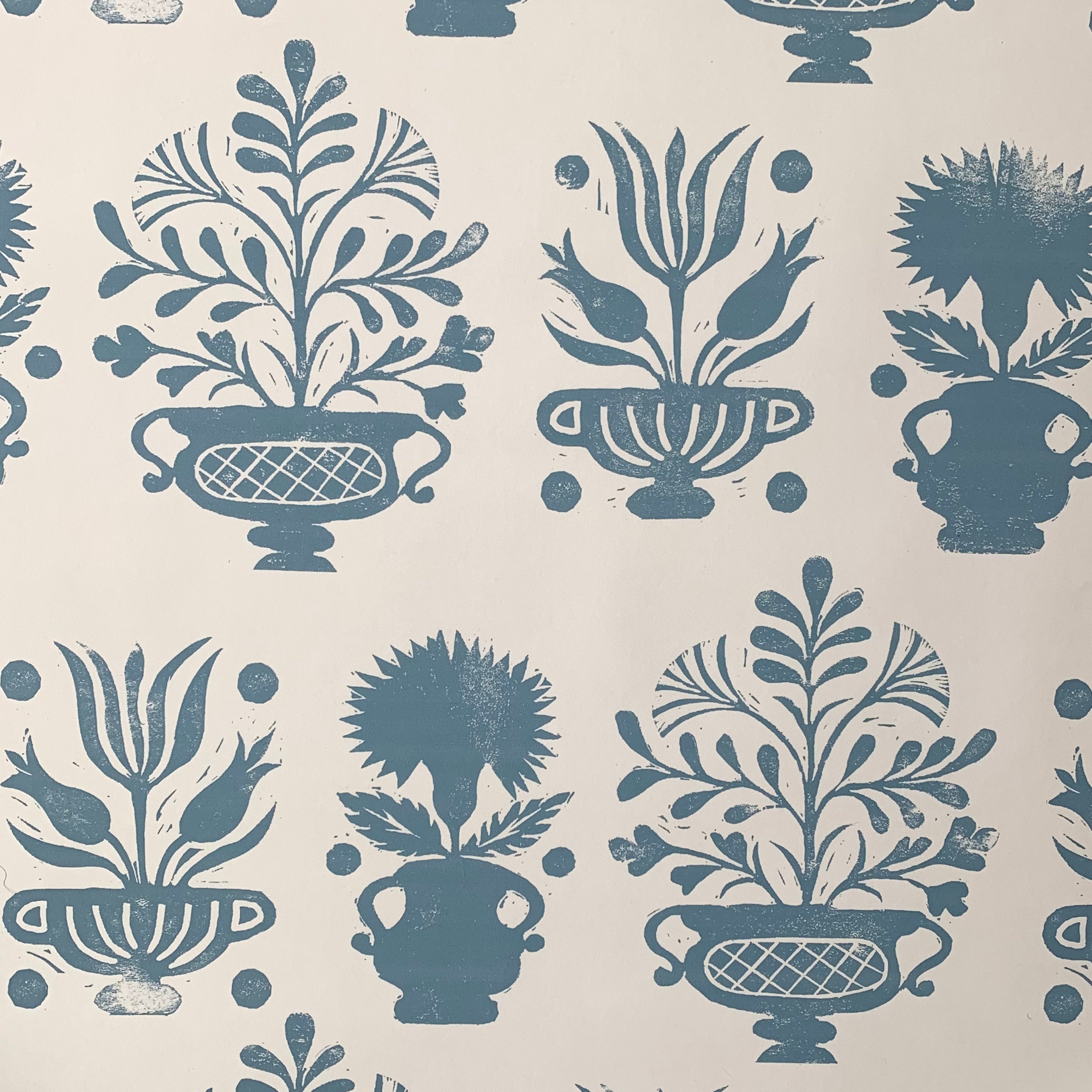 Detail of wallpaper in a repeating vase and plant print in blue on a white field.