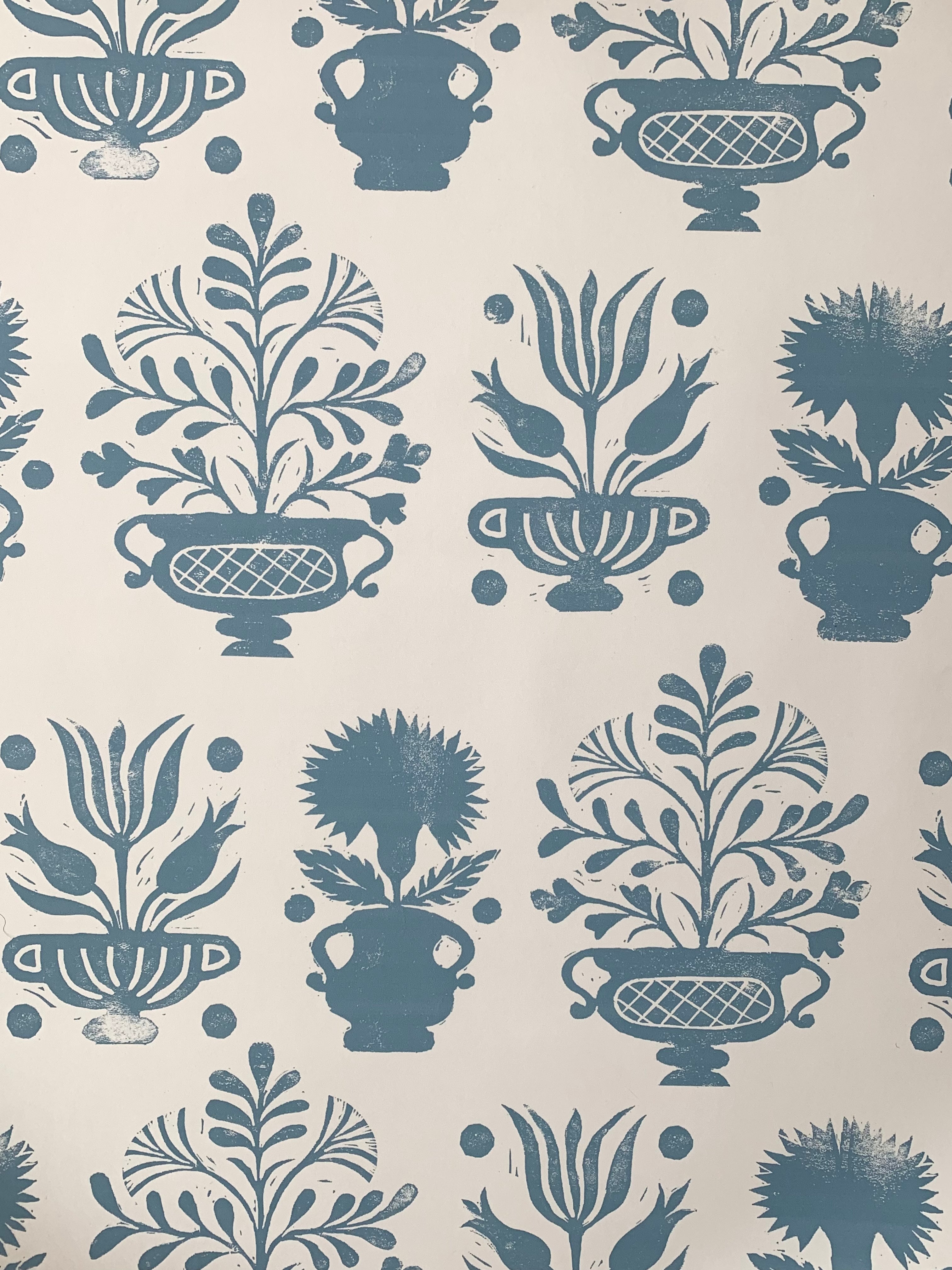 Detail of wallpaper in a repeating vase and plant print in blue on a white field.