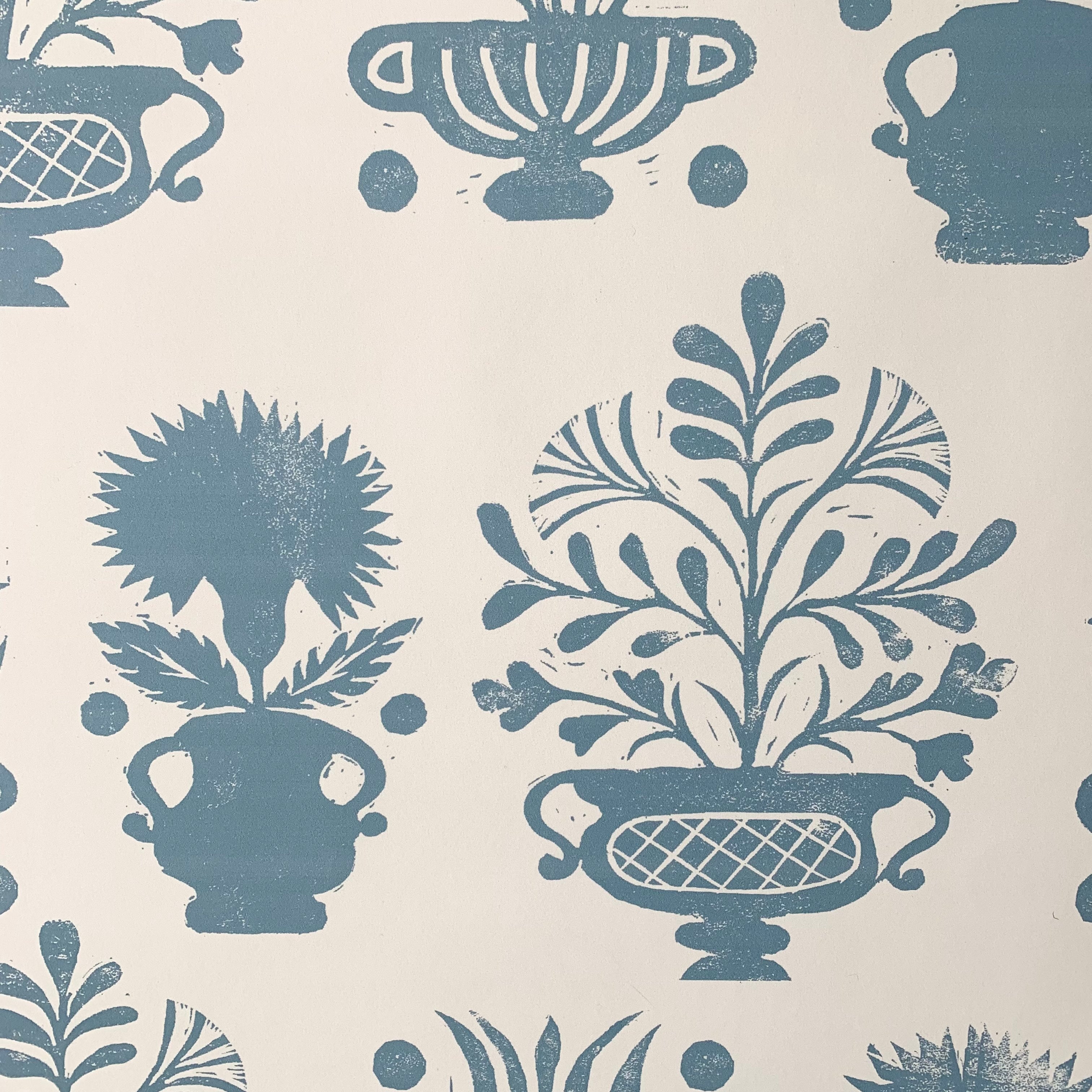 Close-up of wallpaper in a repeating vase and plant print in blue on a white field.