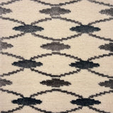 Handknotted rug detail in a diamond lattice pattern in black and grey on a cream field. 