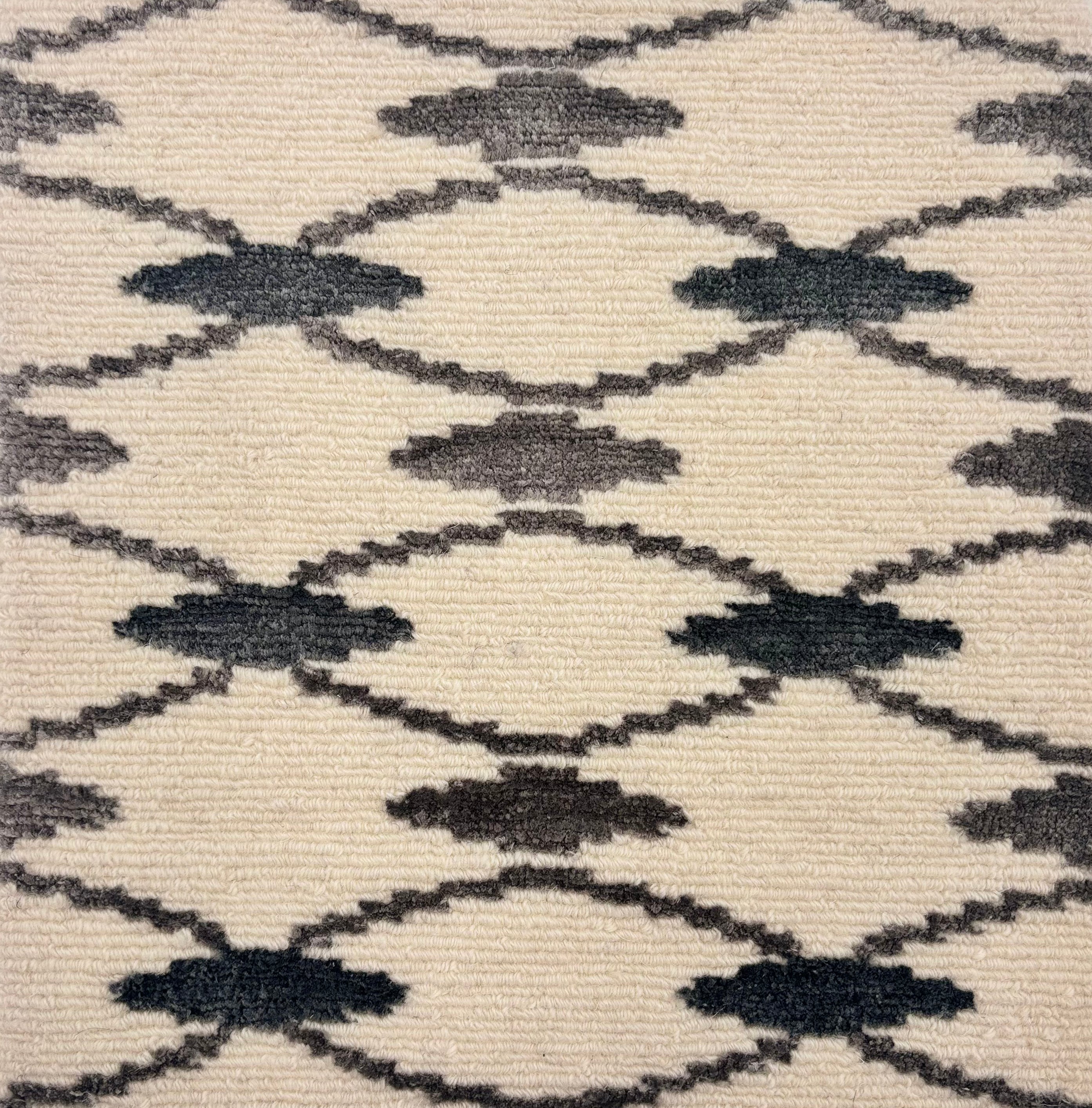 Handknotted rug detail in a diamond lattice pattern in black and grey on a cream field. 