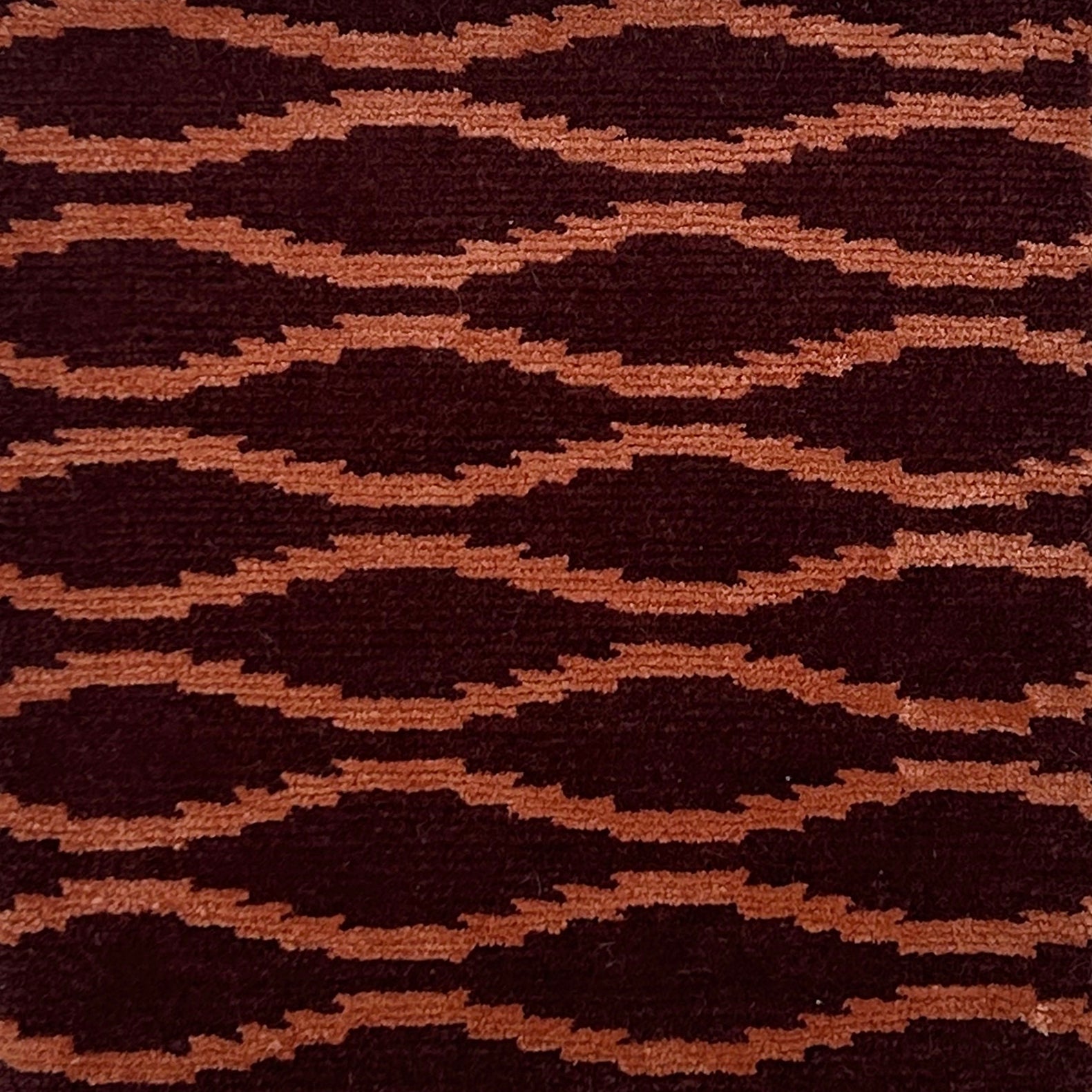 Hand knotted rug with a wavy line in orange on a maroon field. 
