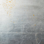 Detail of wallpaper in a minimal gold paint splatter print on a silver field.