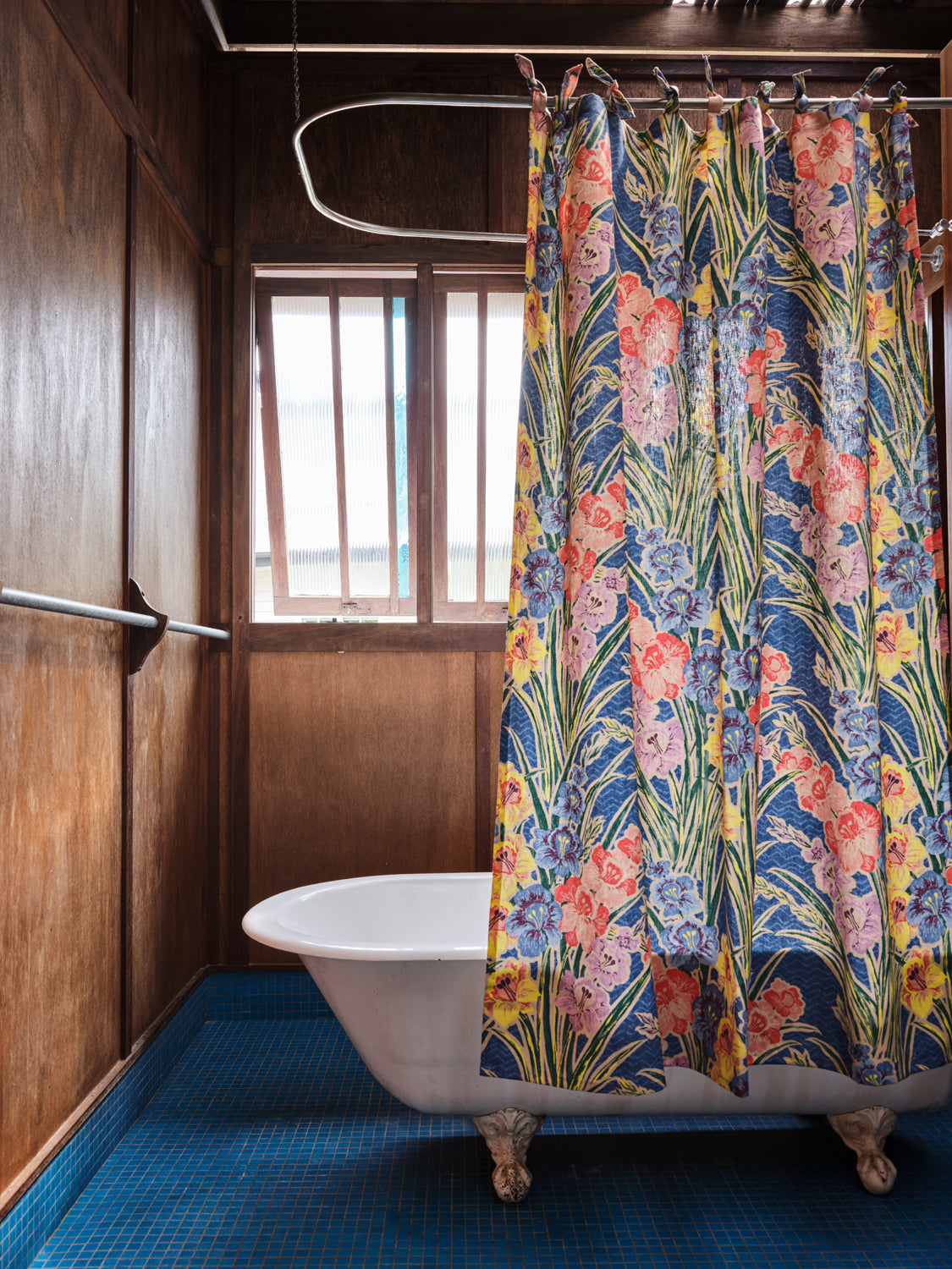 A clawfoot tub with a large-scale floral shower curtain stands in a rustic wooden bathroom.