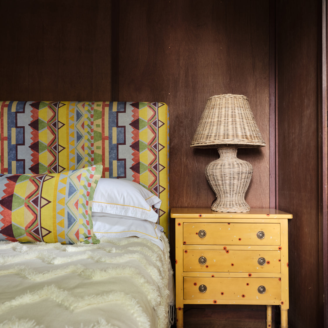 A cozy bedroom tableau with a headboard and throw pillows upholstered in a playful geometric stripe print.