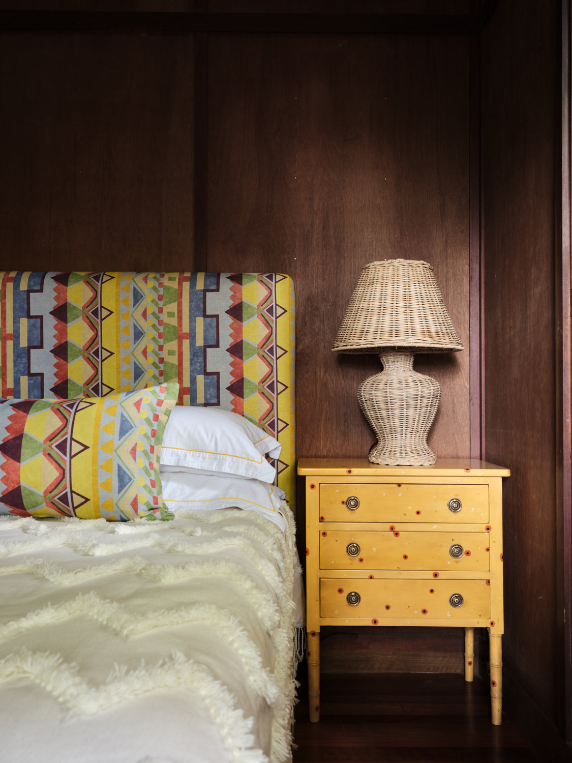 A cozy bedroom tableau with a headboard and throw pillows upholstered in a playful geometric stripe print.