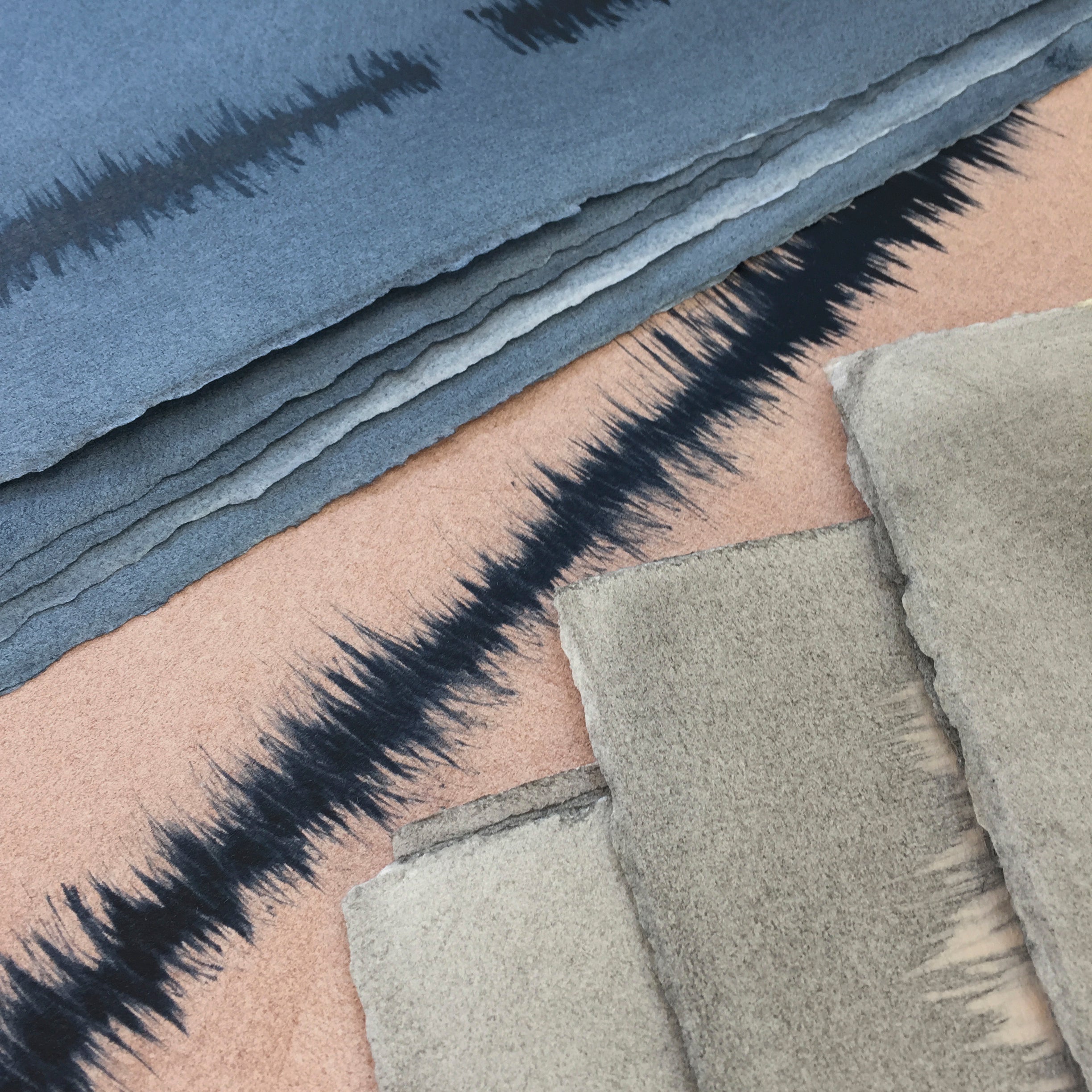 Pile of wallpaper swatches with irregular vibrating linear patterns in blue, tan and gray.