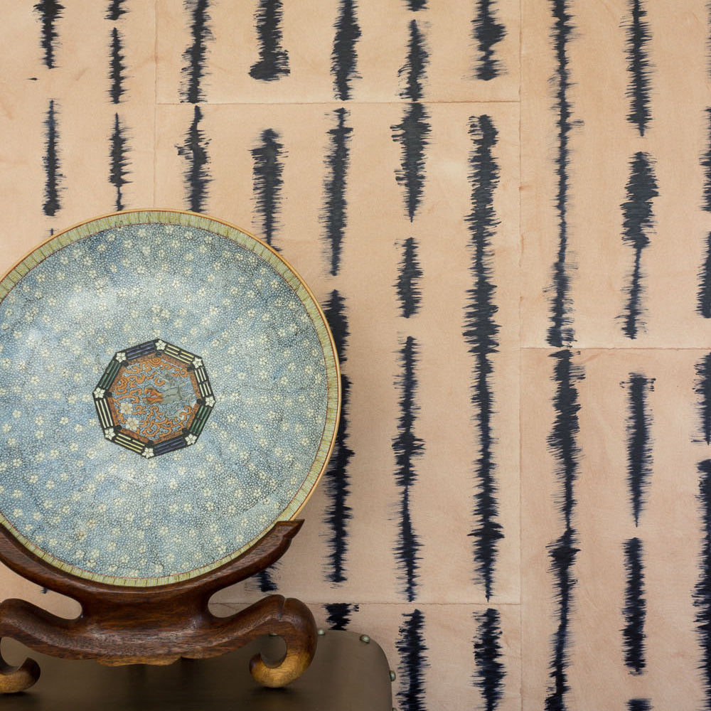 A china plate stands in front of a wall papered in an irregular vibrating linear pattern in navy on a tan field.