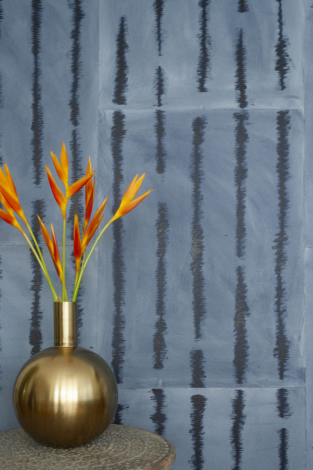 A vase of flowers stands in front of a wall papered in an irregular vibrating linear pattern in navy on a blue field.