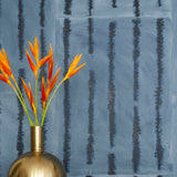 A vase of flowers stands in front of a wall papered in an irregular vibrating linear pattern in navy on a blue field.