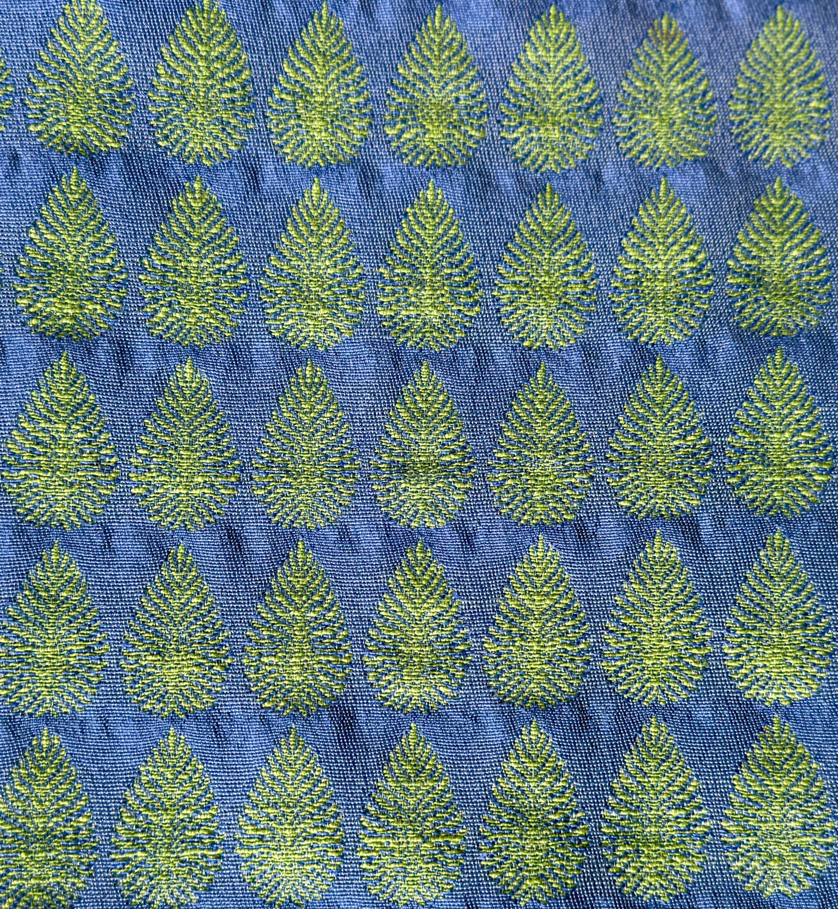 Detail of fabric woven in a repeating leaf print in shades of blue and green.