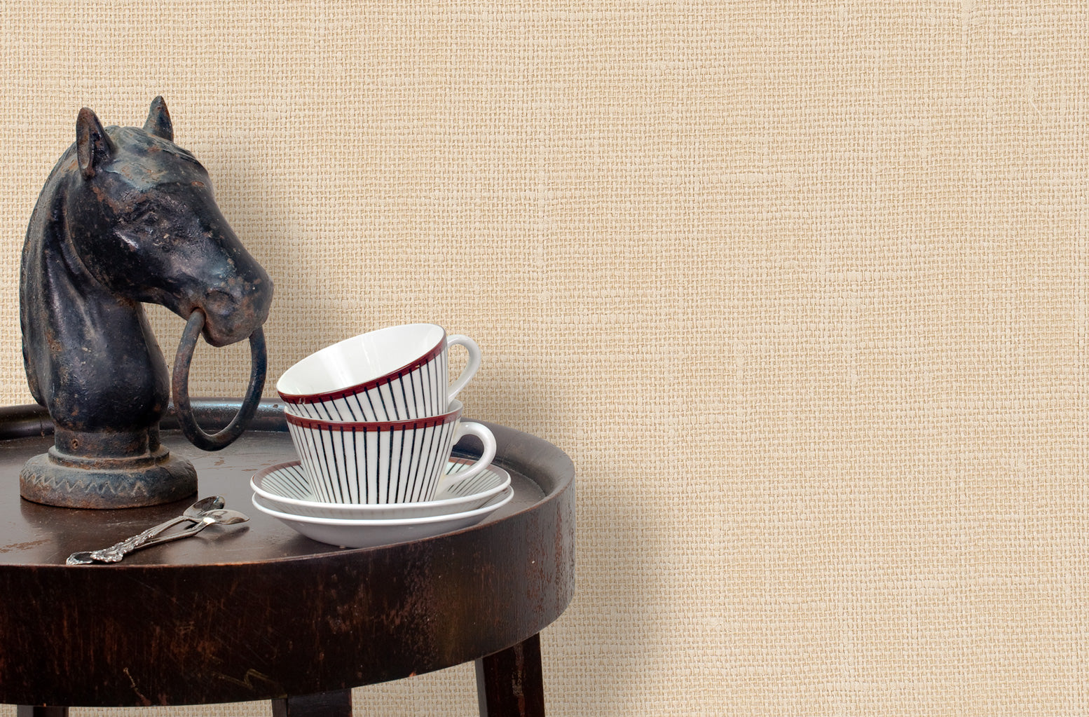 End table with a horse sculpture and tea cups in front of a wall papered in textured cream hemp wallpaper.
