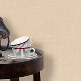 End table with a horse sculpture and tea cups in front of a wall papered in textured cream hemp wallpaper.