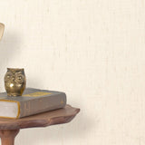 End table with a phone, book and owl sculpture in front of a wall covered in paperweave grasscloth in cream.