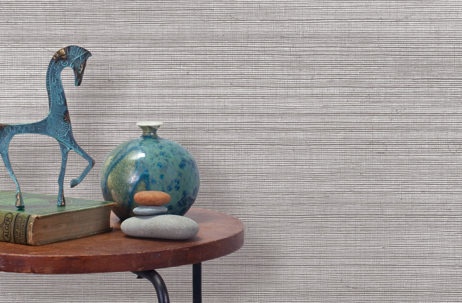 End table with a vase, horse sculpture and stones in front of a wall covered in sisal grasscloth in mottled gray.