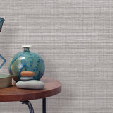 End table with a vase, horse sculpture and stones in front of a wall covered in sisal grasscloth in mottled gray.