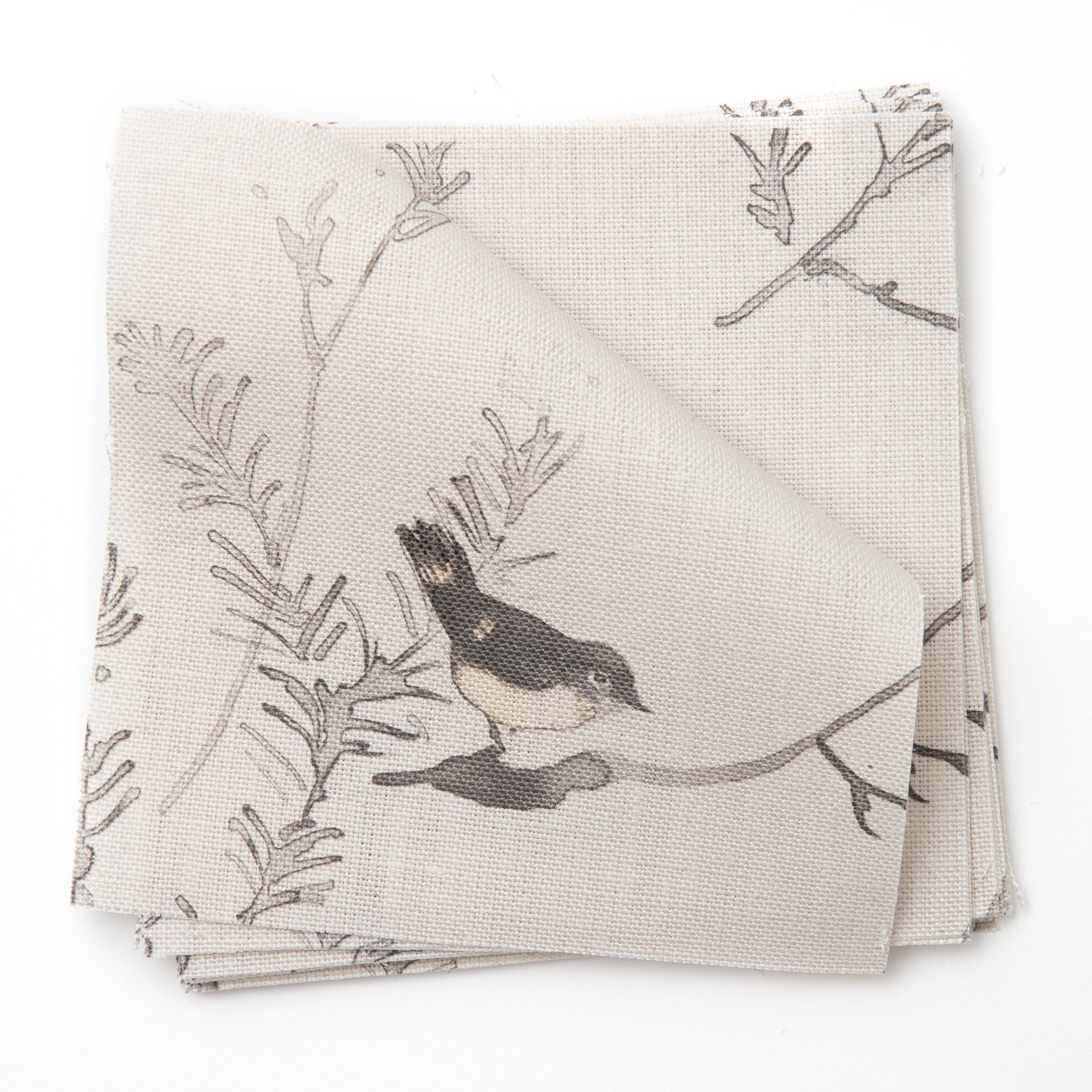 A stack of fabric swatches in a painterly bird and branch pattern in shades of gray on a greige field.