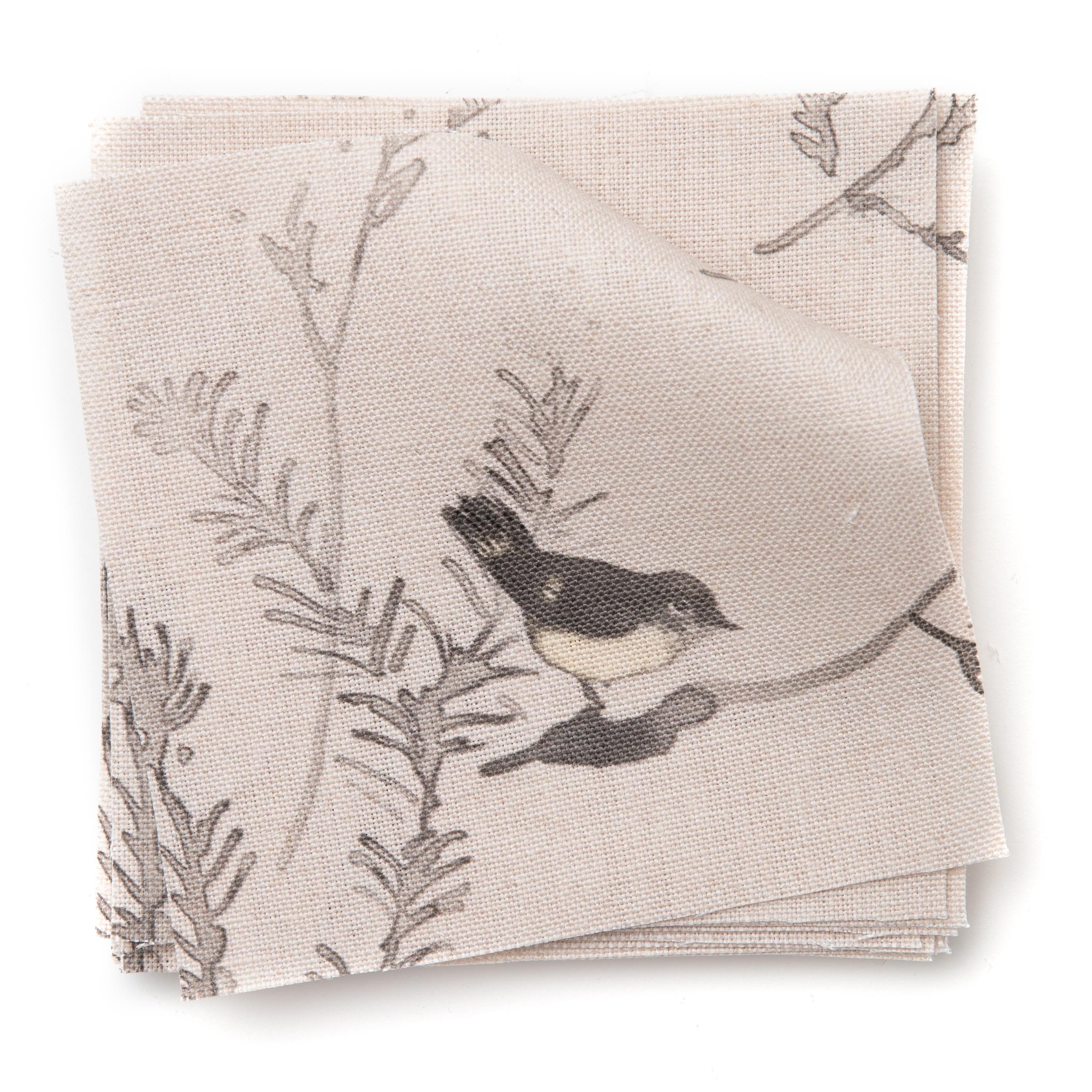 A stack of fabric swatches in a painterly bird and branch pattern in shades of gray on a light pink field.