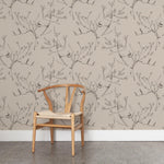 A wooden chair stands in front of a wall papered in a painterly bird and branch pattern in shades of gray on a greige field.