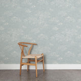 A wooden chair stands in front of a wall papered in a painterly cloud pattern in white on a sky blue field.