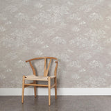 A wooden chair stands in front of a wall papered in a painterly cloud pattern in white on a light gray field.