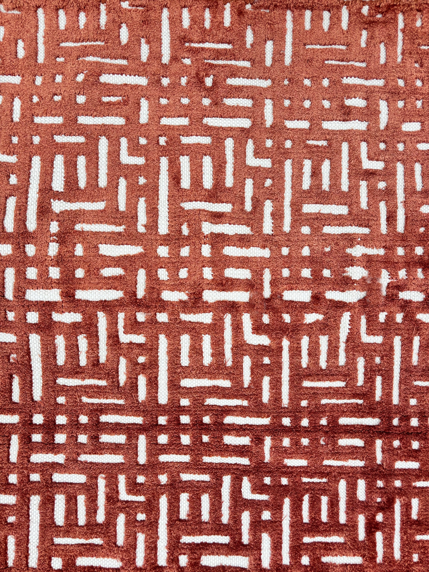 Handknotted rug sample with a geometric lattice pattern in rust red on a white field.