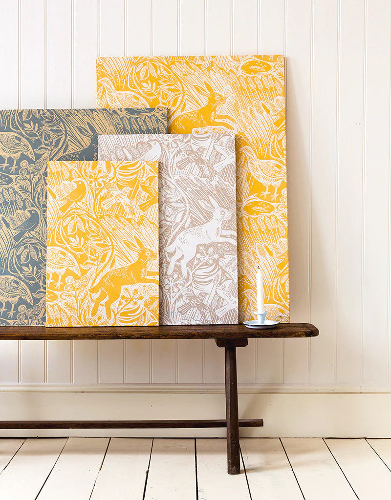 A wooden bench topped with several wallpaper swatches of a playful rabbit and bird print in a variety of colorways.