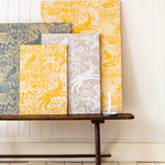 A wooden bench topped with several wallpaper swatches of a playful rabbit and bird print in a variety of colorways.