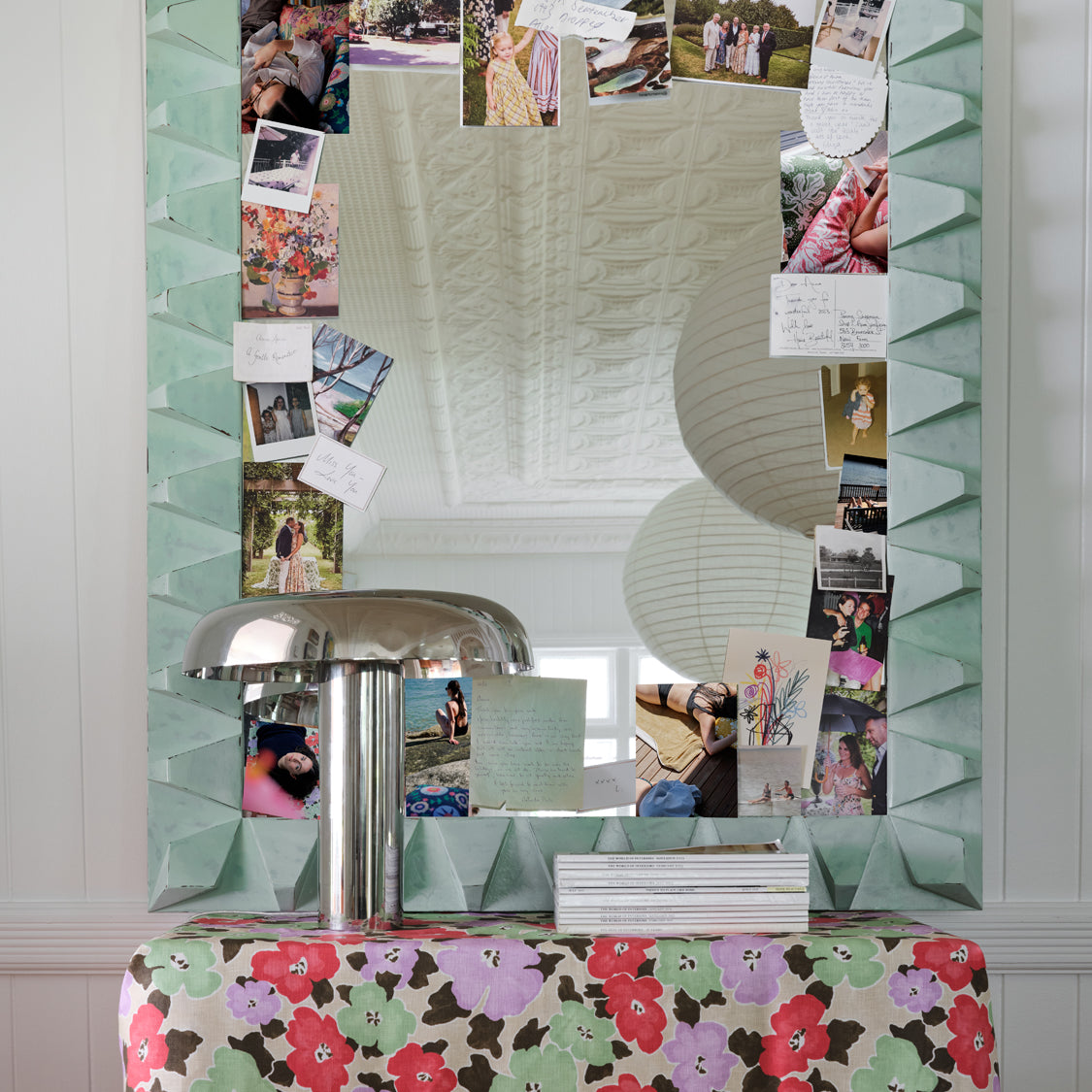 A mirror cluttered with photos and notes rests on a table draped in painterly floral fabric yardage.